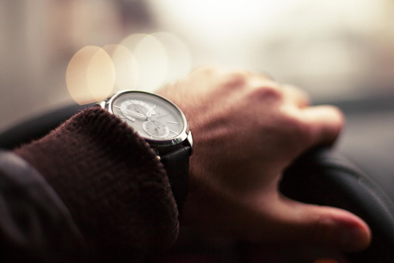 Driver’s hand and watch on the steering wheel, city lights blurred beyond